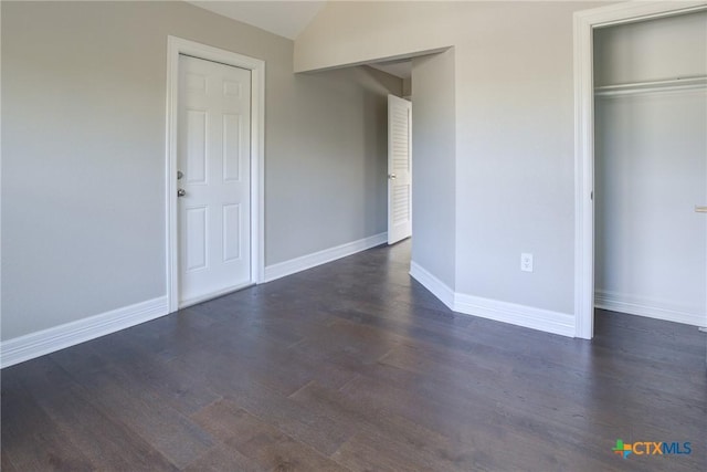 unfurnished bedroom with dark hardwood / wood-style floors, vaulted ceiling, and a closet