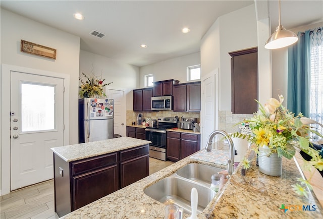 kitchen featuring decorative light fixtures, sink, light stone counters, and stainless steel appliances