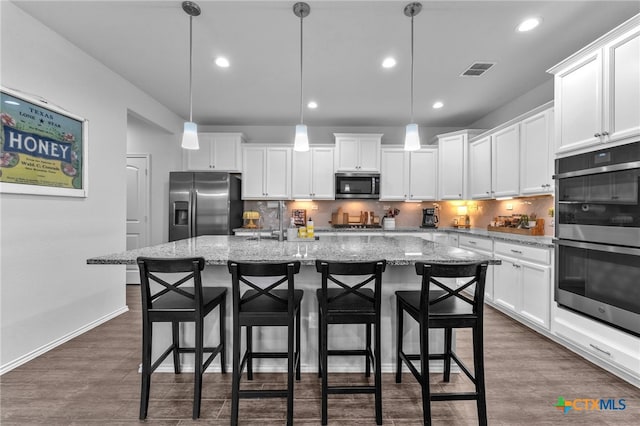 kitchen featuring appliances with stainless steel finishes, a kitchen island with sink, decorative light fixtures, white cabinetry, and a breakfast bar area