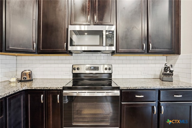 kitchen with dark brown cabinetry, stainless steel appliances, tasteful backsplash, and light stone countertops