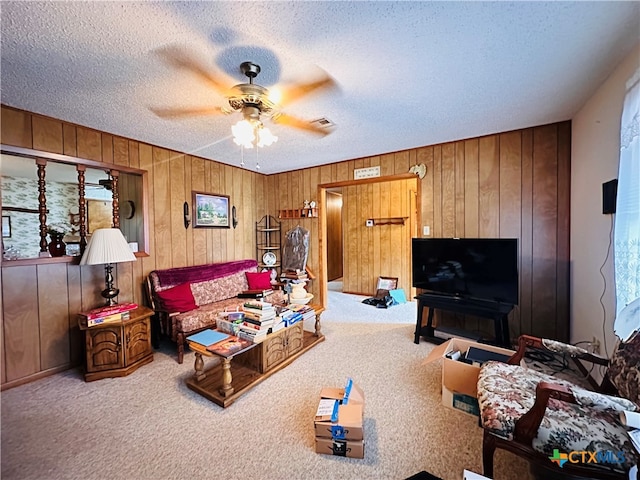 carpeted living room with a textured ceiling, wood walls, and ceiling fan