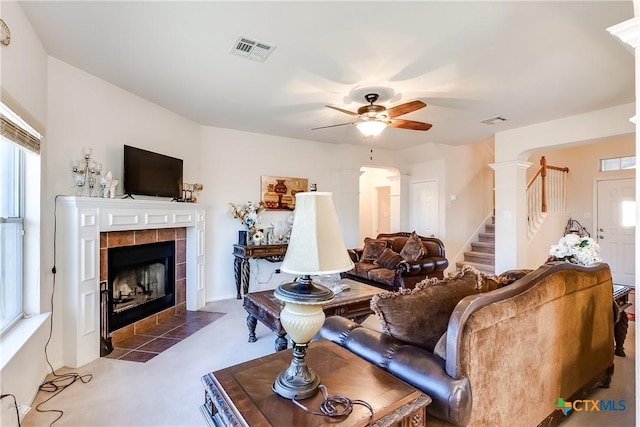 carpeted living room with a tiled fireplace, ceiling fan, and ornate columns