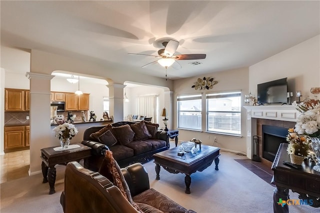 carpeted living room with ceiling fan, a tile fireplace, and ornate columns