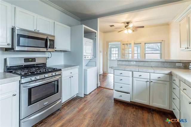 kitchen featuring stacked washing maching and dryer, white cabinetry, stainless steel appliances, crown molding, and dark wood-type flooring