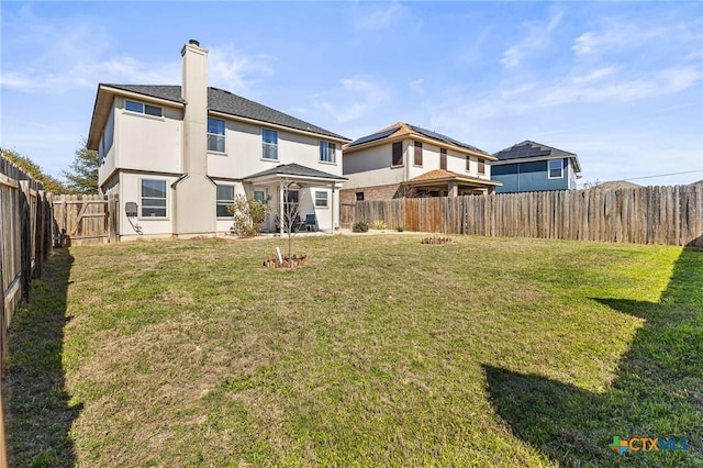 rear view of house with a chimney, a fenced backyard, a lawn, and stucco siding