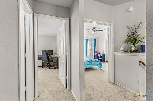 hallway featuring a textured wall, carpet, and baseboards