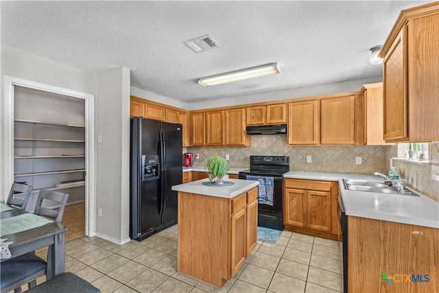 kitchen featuring light tile patterned floors, under cabinet range hood, a sink, visible vents, and black appliances