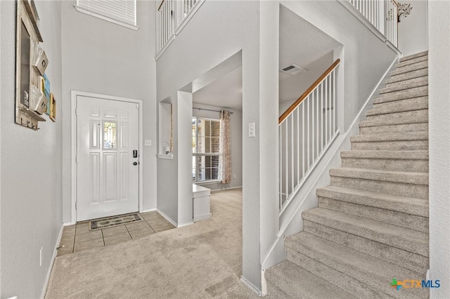 carpeted foyer featuring baseboards, visible vents, a high ceiling, and stairs