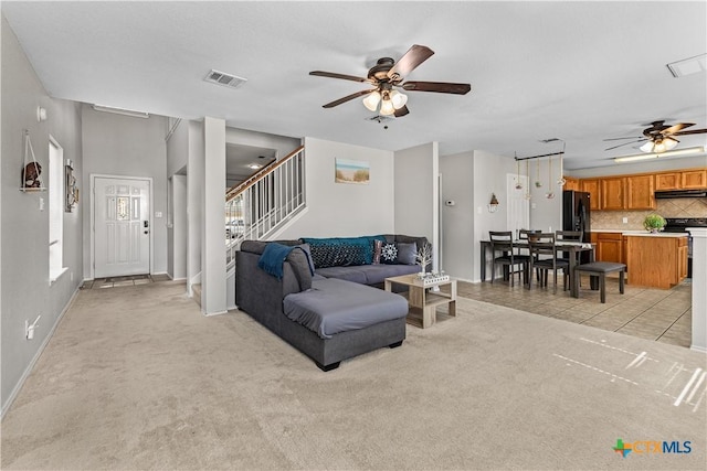 living area with stairway, light colored carpet, ceiling fan, and visible vents