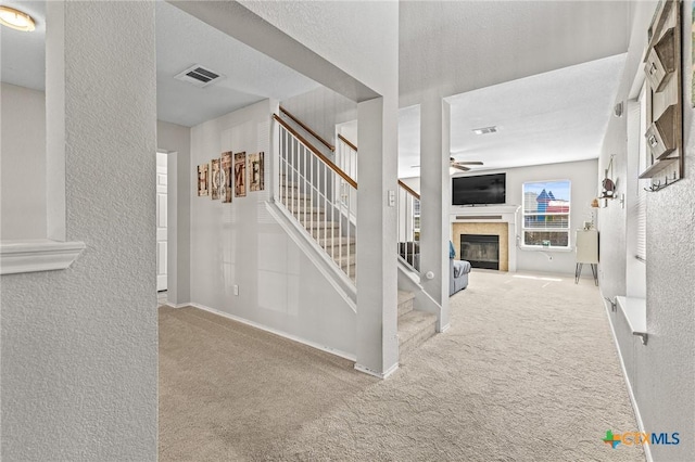 staircase with ceiling fan, a textured wall, a tile fireplace, carpet floors, and visible vents