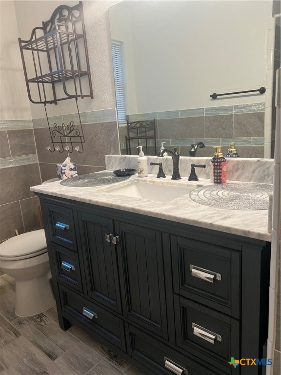 bathroom featuring wood-type flooring, vanity, toilet, and tile walls