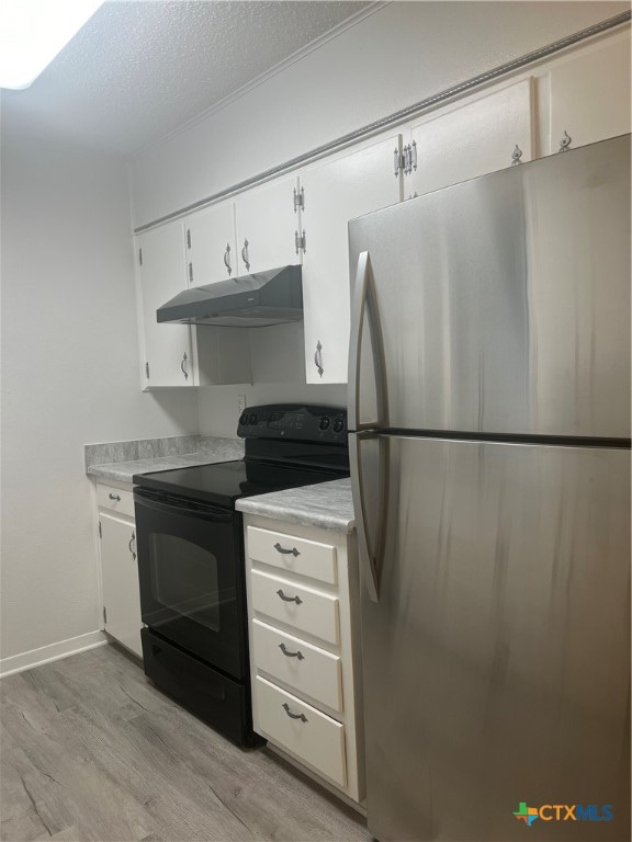 kitchen featuring black range with electric cooktop, stainless steel fridge, a textured ceiling, white cabinets, and light hardwood / wood-style flooring