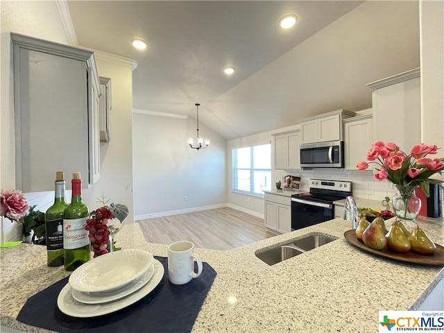 kitchen with stainless steel appliances, light stone counters, lofted ceiling, and a notable chandelier