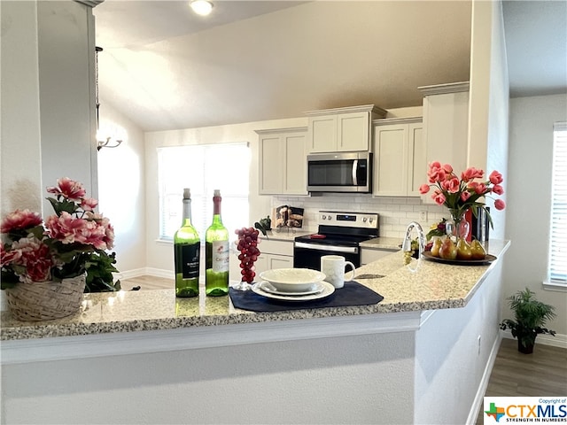 kitchen with lofted ceiling, light stone counters, hardwood / wood-style flooring, white cabinetry, and appliances with stainless steel finishes