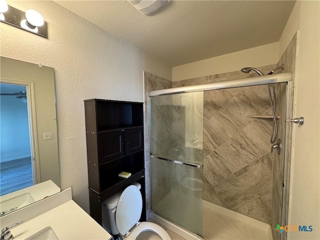 bathroom with a textured ceiling, toilet, a shower with door, and vanity