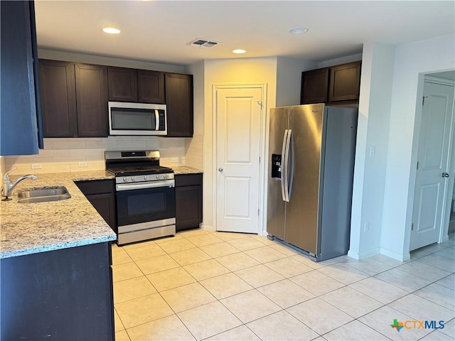 kitchen with appliances with stainless steel finishes, decorative backsplash, dark brown cabinets, light stone countertops, and sink