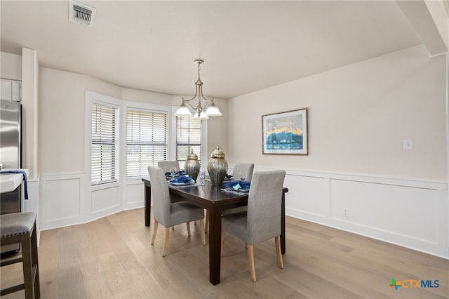 dining space with a decorative wall, a chandelier, light wood-style flooring, and visible vents