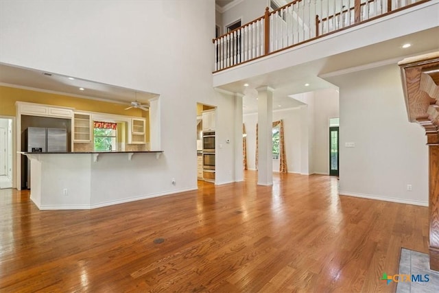 11740 Stinnett Mill Rd, Salado, TX 76571 - unfurnished living room with a ceiling fan, wood finished floors, a high ceiling, crown molding, and ornate columns