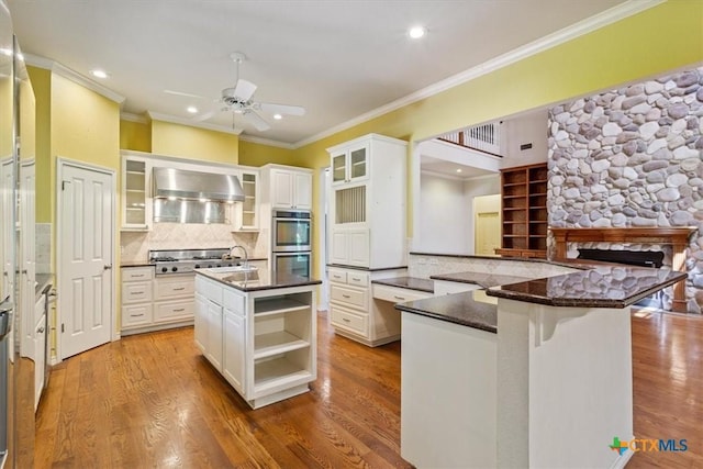 11740 Stinnett Mill Rd, Salado, TX 76571 - kitchen featuring wall chimney range hood, stainless steel appliances, ornamental molding, ceiling fan, and wood finished floors