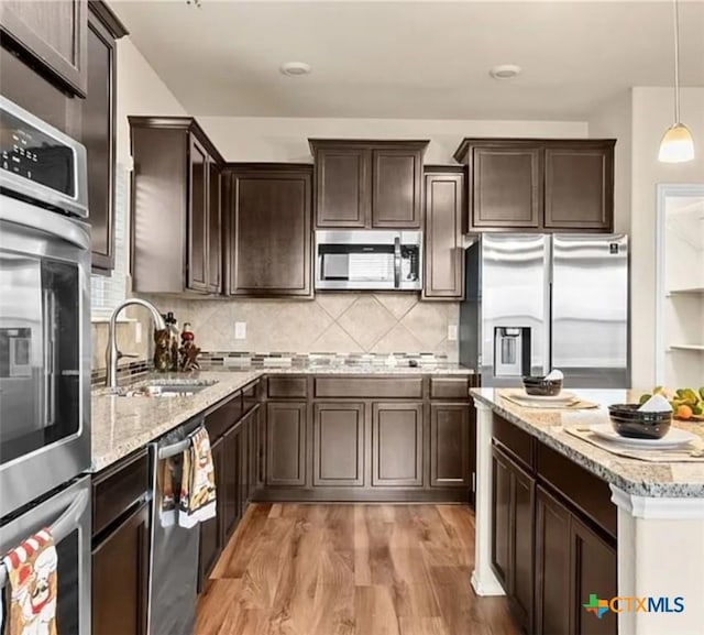 5561 Perdita Dr, Belton, TX 76513 - kitchen with light stone counters, stainless steel appliances, dark brown cabinets, a sink, and light wood-type flooring