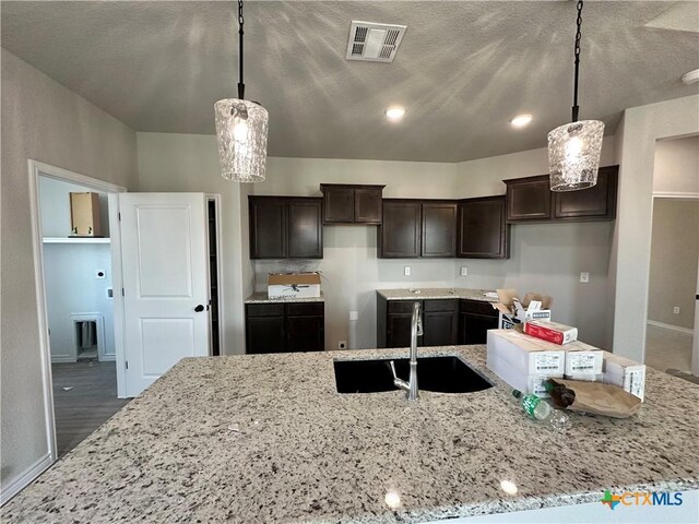 2598 Settlers Oak Dr, Belton, TX 76513 - kitchen featuring a sink, dark brown cabinets, light stone countertops, baseboards, and hanging light fixtures