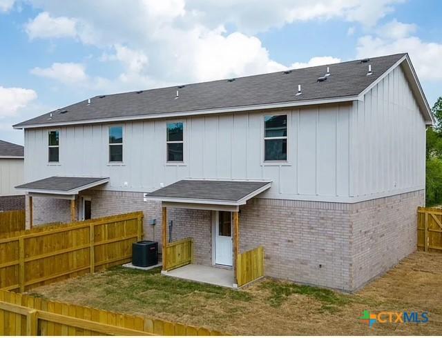 rear view of property with brick siding, central AC, board and batten siding, and fence