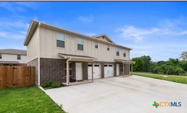 view of front of home featuring an attached garage, board and batten siding, fence, a front lawn, and driveway