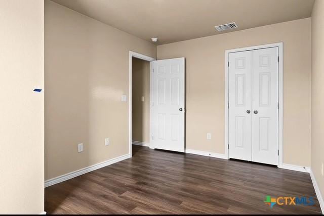 unfurnished bedroom with visible vents, baseboards, a closet, and dark wood finished floors