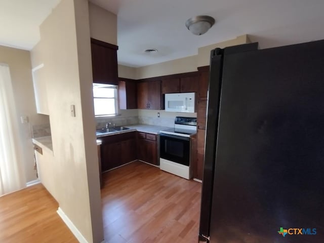 kitchen with sink, light hardwood / wood-style flooring, range with electric cooktop, dark brown cabinetry, and black fridge