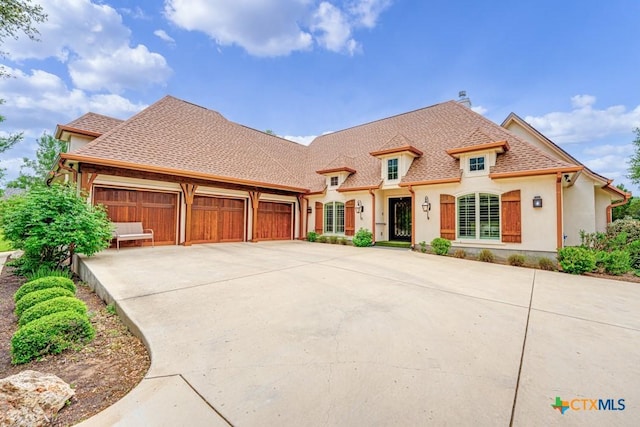 french country home with stucco siding, driveway, a shingled roof, and a garage