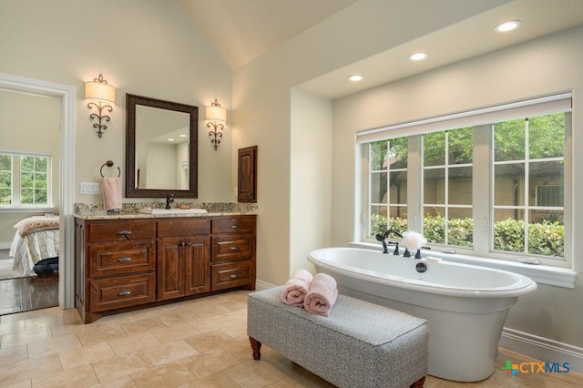 bathroom featuring a freestanding bath, vanity, baseboards, ensuite bathroom, and vaulted ceiling