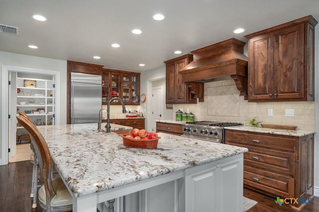 kitchen featuring a sink, stove, built in refrigerator, visible vents, and custom exhaust hood