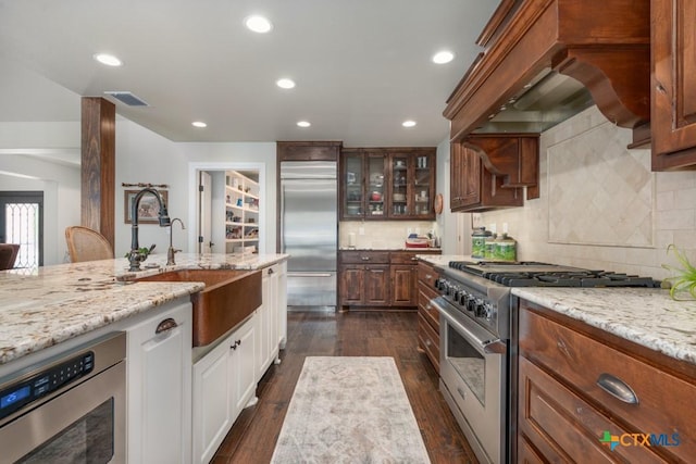 kitchen with a sink, premium appliances, light stone countertops, and glass insert cabinets