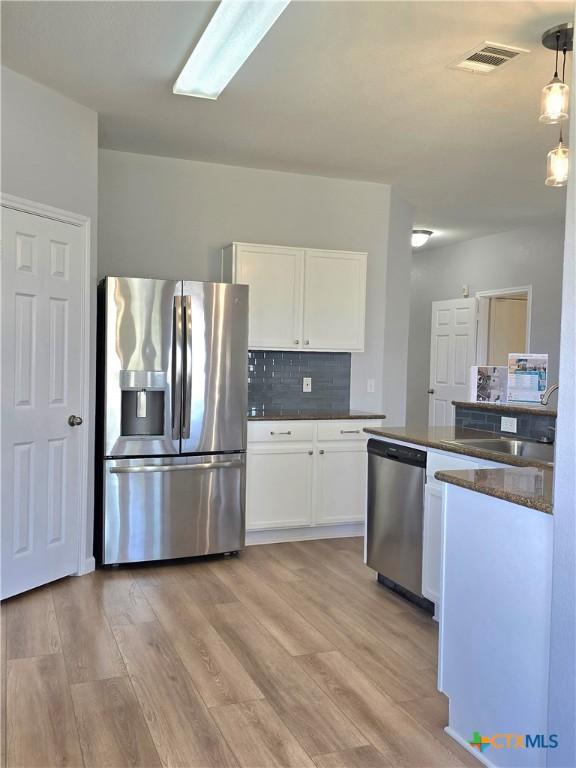 3300 Porter Creek Cv, Round Rock, TX 78665 - kitchen with stainless steel appliances, white cabinets, light wood-type flooring, a sink, and visible vents