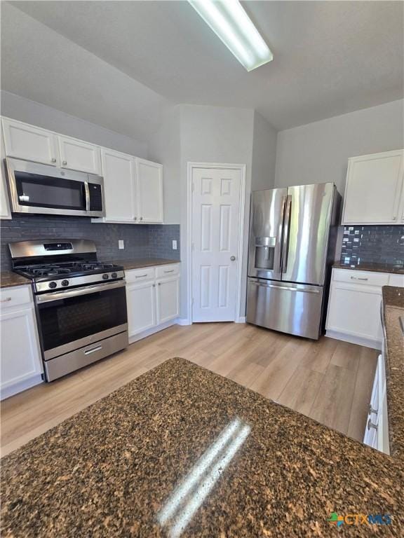 3300 Porter Creek Cv, Round Rock, TX 78665 - kitchen featuring decorative backsplash, dark stone countertops, light wood-type flooring, white cabinetry, and appliances with stainless steel finishes