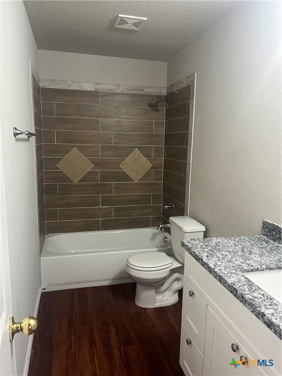 full bathroom featuring toilet, tiled shower / bath, a textured ceiling, hardwood / wood-style flooring, and vanity