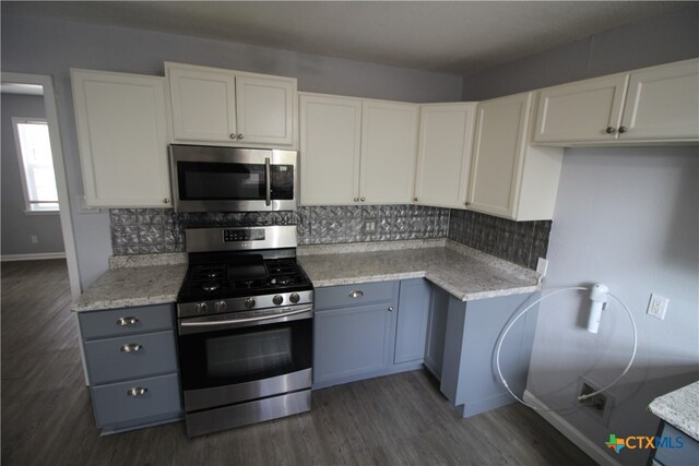 kitchen with stainless steel appliances, decorative backsplash, light stone countertops, white cabinets, and dark hardwood / wood-style flooring