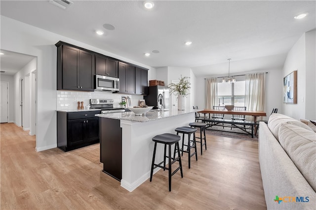 kitchen featuring a kitchen breakfast bar, appliances with stainless steel finishes, an island with sink, and light hardwood / wood-style flooring