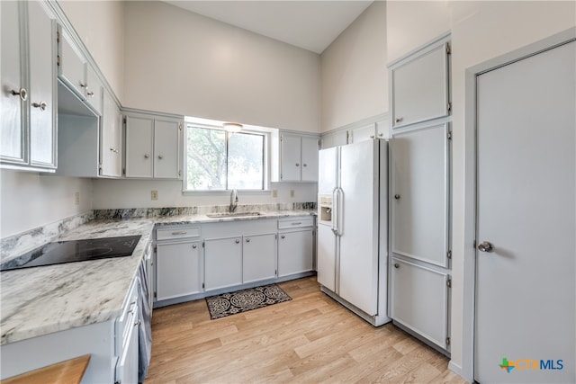 kitchen featuring light stone counters, white fridge with ice dispenser, sink, black electric cooktop, and light hardwood / wood-style flooring