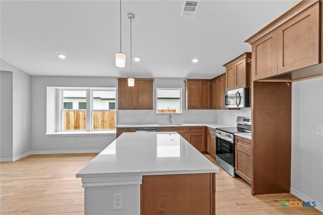 kitchen with a kitchen island, a wealth of natural light, light hardwood / wood-style floors, and stainless steel appliances