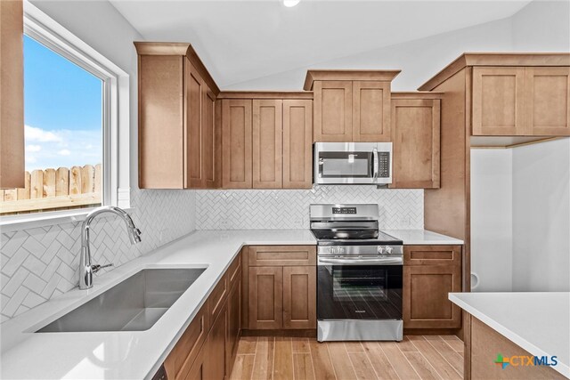 kitchen with sink, decorative backsplash, appliances with stainless steel finishes, light hardwood / wood-style flooring, and vaulted ceiling