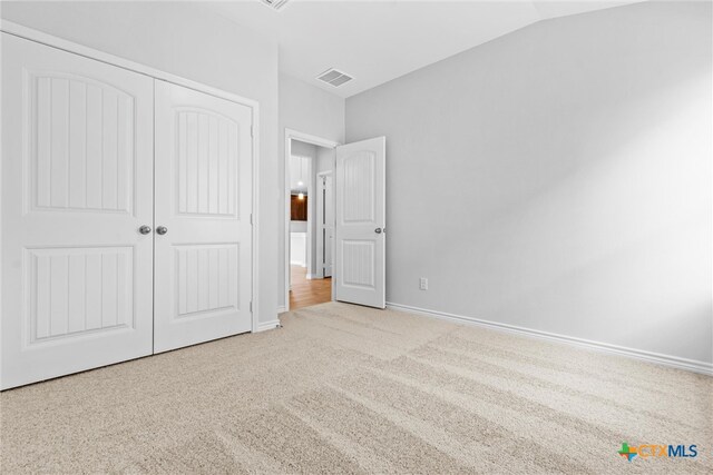 unfurnished bedroom featuring light carpet, a closet, and lofted ceiling