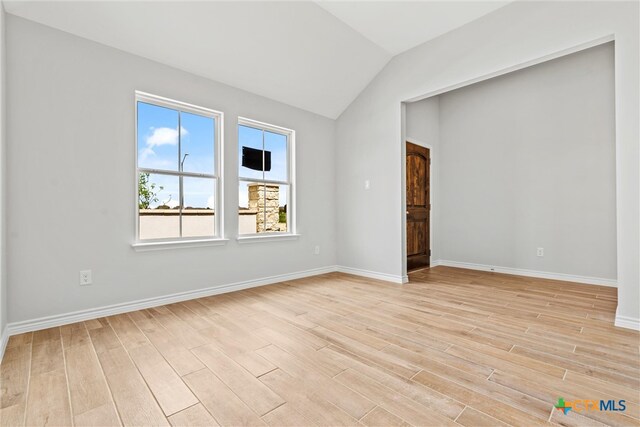 empty room with light hardwood / wood-style floors and vaulted ceiling