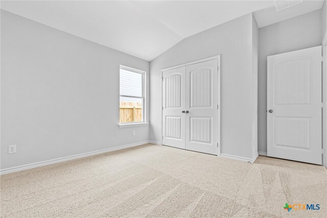 unfurnished bedroom featuring light colored carpet, lofted ceiling, and a closet