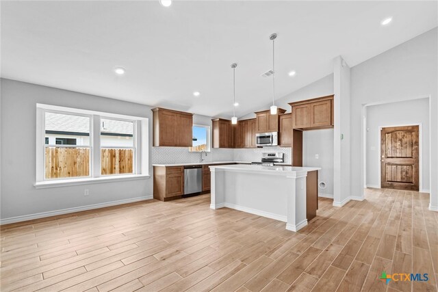 kitchen with light wood-type flooring, appliances with stainless steel finishes, decorative light fixtures, and a center island