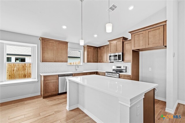 kitchen featuring a center island, backsplash, appliances with stainless steel finishes, decorative light fixtures, and light hardwood / wood-style flooring