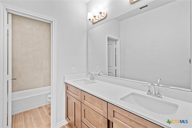 full bathroom with tiled shower / bath combo, vanity, hardwood / wood-style flooring, and toilet