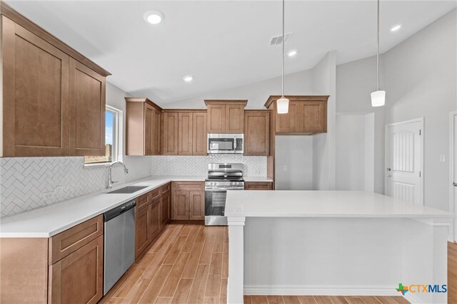 kitchen featuring stainless steel appliances, hanging light fixtures, sink, vaulted ceiling, and a center island