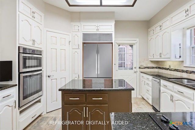 kitchen featuring white cabinets, a center island, stainless steel appliances, and dark stone counters