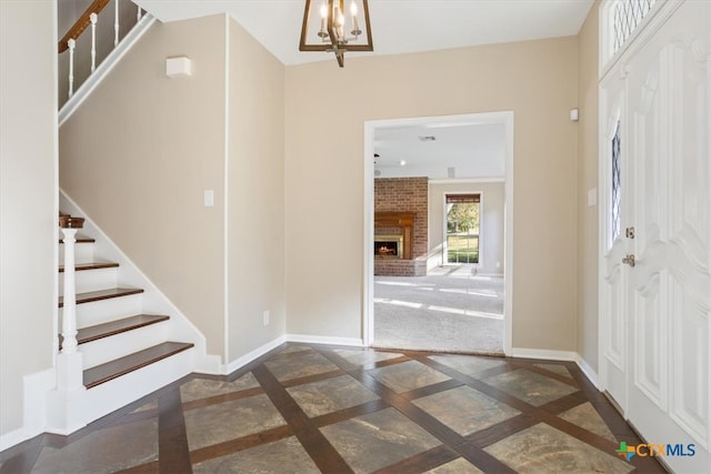 foyer entrance featuring a brick fireplace and a notable chandelier